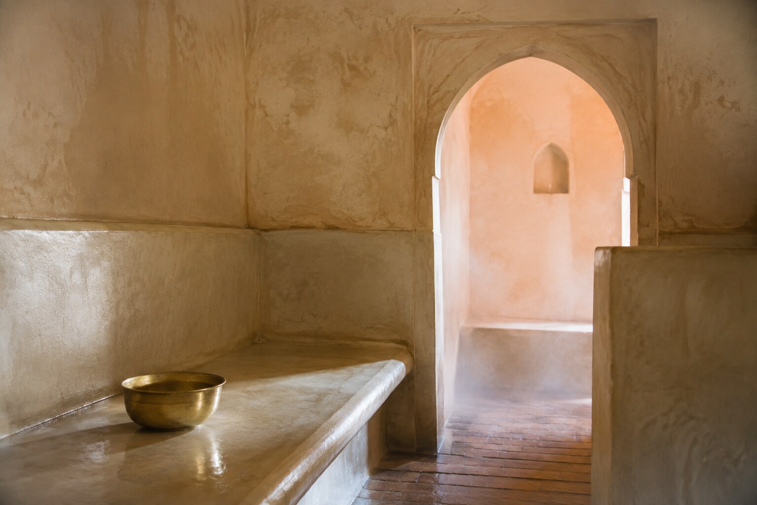 Warm tadelakt walls and a simple water bowl inside a Moroccan hammam